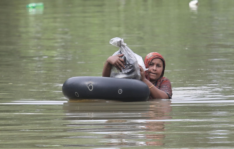 ডুবে যাওয়া ঘর থেকে মালামাল নিয়ে টিউবে ভর করে নিরাপদ স্থানের দিকে যাচ্ছেন এক নারী। গতকাল ফেনী সদরের খাইয়ারা বাজার এলাকায়